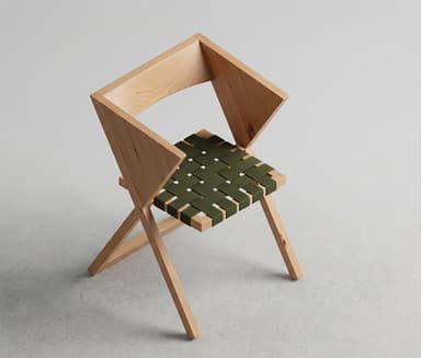 A minimalist folding chair featuring a light-toned wooden frame and an olive green woven webbing seat and backrest. The chair is depicted in a partially open or folded state, suggesting its space-saving design. Its clean lines and simple construction highlight a modern aesthetic. — 3D model