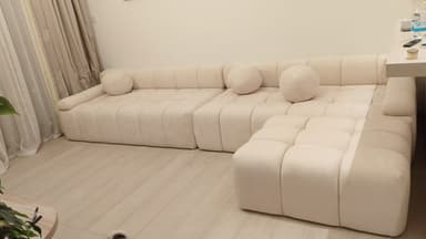 A modular sectional sofa with a tufted, upholstered design. It features a light cream or off-white fabric and includes multiple square seat cushions and back cushions, along with decorative spherical throw pillows. The configuration appears to be a chaise lounge attached to a longer sofa section. — 3D model