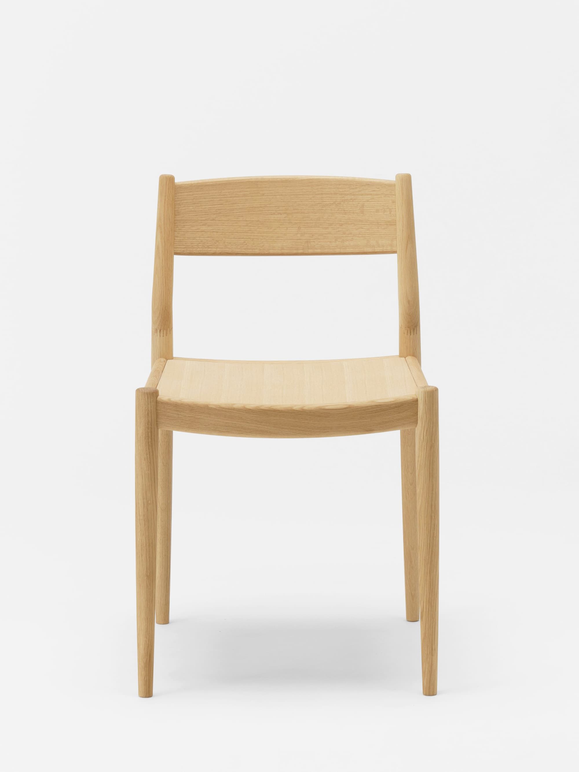 A minimalist wooden chair with a gently curved backrest and seat. The chair features four tapered legs and a simple, unadorned frame constructed from light-colored wood. — 3D model