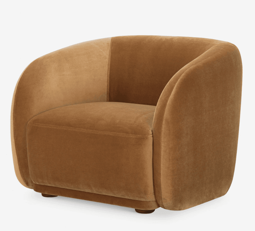 A fully upholstered barrel-shaped accent chair in a warm camel-colored velvet fabric. The chair features a continuous curved back and arms, creating a cozy, enveloping silhouette. Visible double-stitched seams define the panels of the upholstery, and the chair rests on small, recessed wooden feet. — 3D model