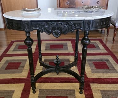 An oval console table with a white marble top and a black, ornately carved wooden base and legs. The base features intricate scrollwork and beading, and the legs are turned and shaped with bulbous sections. A decorative stretcher connects the legs. — 3D model