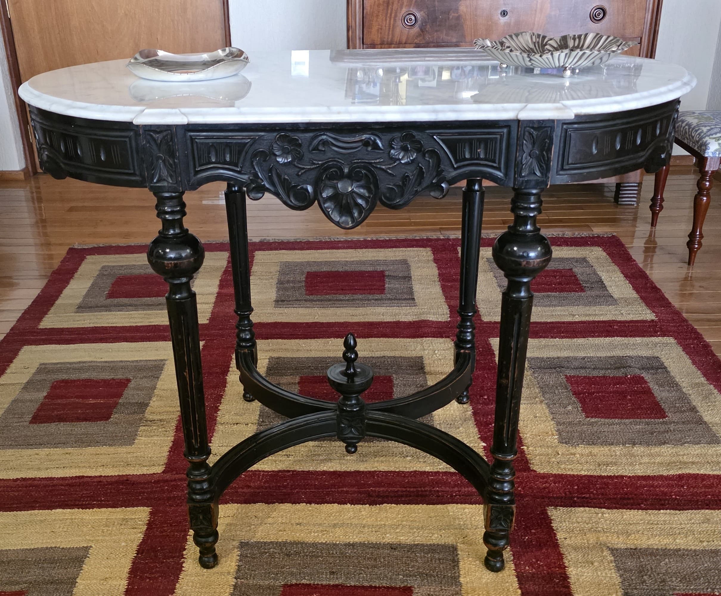 An oval console table with a white marble top and a black, ornately carved wooden base and legs. The base features intricate scrollwork and beading, and the legs are turned and shaped with bulbous sections. A decorative stretcher connects the legs. — 3D model