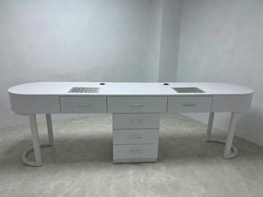 A modern, sleek, white double manicure table featuring an elongated, oval-shaped tabletop. It incorporates two integrated ventilation grates, two circular openings (likely for cords or lights), and ample storage provided by multiple drawers, including a central cabinet unit with four drawers and two smaller drawers on either side of the ventilation grates. The table stands on two stylish U-shaped metal legs and a central cabinet base. — 3D model
