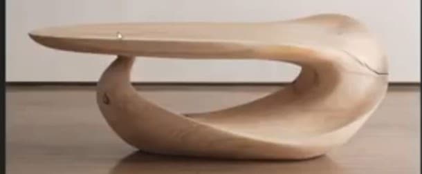A low, sculptural coffee table characterized by its fluid, biomorphic shape crafted entirely from light-toned wood. The design features a continuous, seamless form where the tabletop gently curves downwards to create the base, eliminating distinct legs and offering a visually striking, organic silhouette. — 3D model
