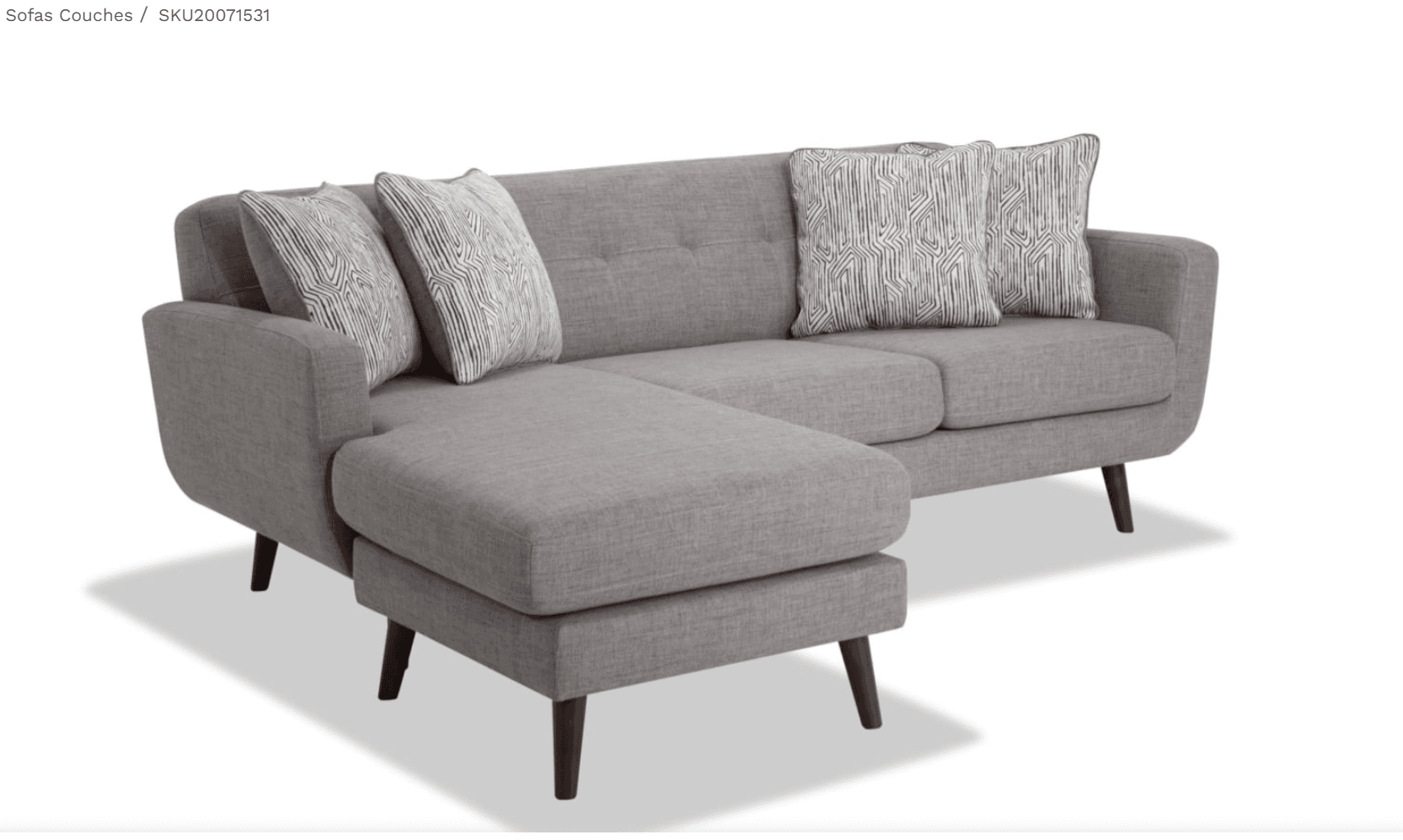 A contemporary gray fabric sectional sofa featuring a reversible chaise lounge. The sofa has clean lines, rounded armrests, and is supported by splayed, tapered dark wooden legs. The backrest includes subtle button tufting, and it comes with multiple loose back cushions and two patterned throw pillows. — 3D model