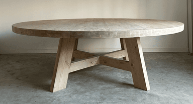 A round dining table with a thick, solid wood top and a substantial base constructed from heavy timber. The base features four angled legs connected by a cross-brace structure, providing stability and a rustic aesthetic. — 3D model