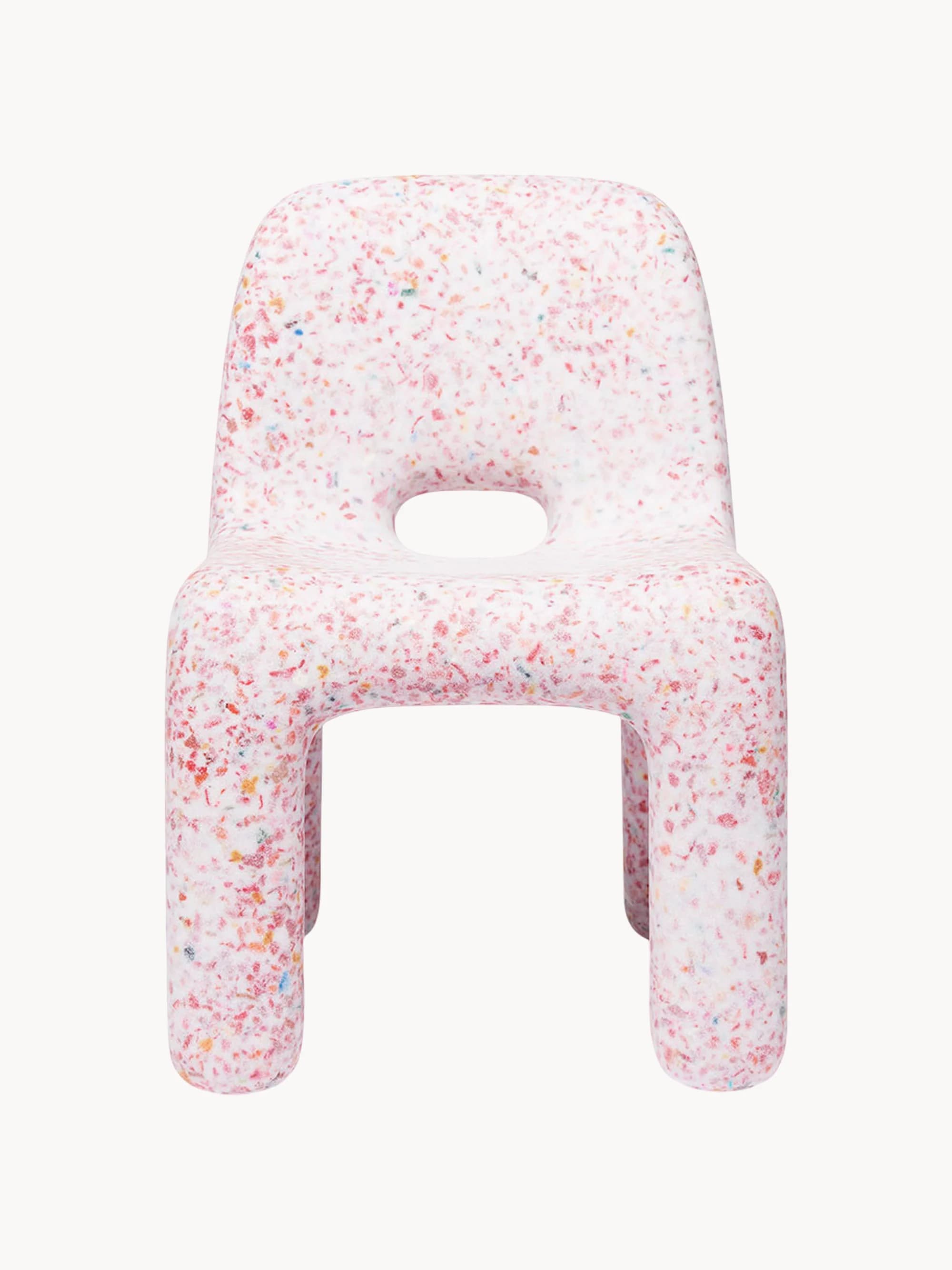 A small, child-sized chair made entirely from a single molded piece of recycled plastic, featuring a distinctive speckled or confetti-like pattern. The chair is predominantly white with multi-colored fragments (red, orange, yellow, blue, green) embedded throughout the material. It has a simple, monolithic design with rounded edges and a backrest, and an oval cutout in the seat. — 3D model