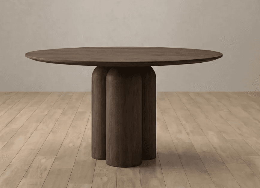 A contemporary round dining table crafted from dark wood, featuring a thick tabletop and a distinctive sculptural pedestal base composed of three large, rounded vertical columns. — 3D model