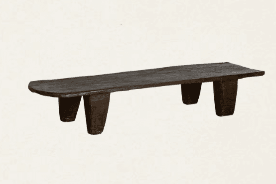 A rustic, dark wooden bench featuring an elongated, flat top and four sturdy, tapered legs. The material appears to be solid, roughly carved wood with a deeply aged or stained dark brown finish, presenting an organic and primitive aesthetic. — 3D model