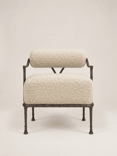 An accent chair featuring a dark, hammered or forged metal frame and upholstered in a light-colored, textured boucle-like fabric. The design includes a separate cylindrical bolster for the backrest and a rectangular cushion for the seat. The metal frame forms minimal armrests and sturdy, tapered legs with small feet. The overall aesthetic is modern and artisanal. — 3D model