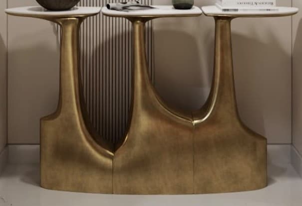A contemporary console table featuring three oval, white marble tops with grey veining, supported by a single, continuous, sculptural base made of brass-finished metal. The base exhibits a fluid, abstract design with three upward curves that meet the underside of each tabletop. — 3D model