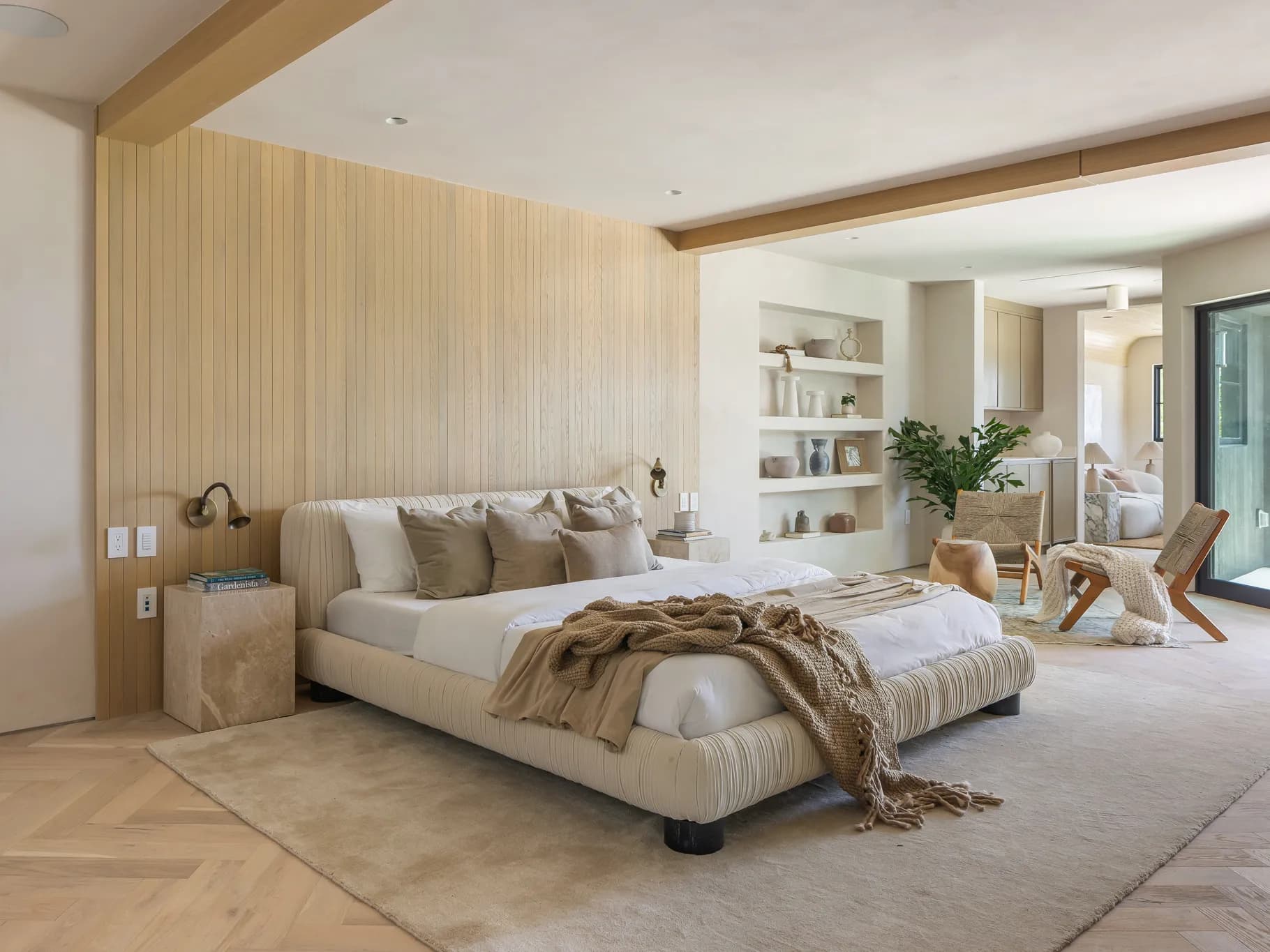 A modern upholstered bed frame with a channel-tufted headboard and side rails. The bed is dressed with white sheets, beige throw pillows, and a textured beige throw blanket with fringe. It sits on short, dark legs. — 3D model