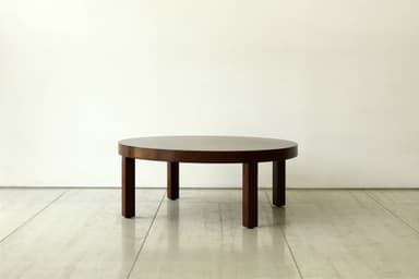 A minimalist round coffee table crafted from dark wood, featuring a thick circular top supported by four sturdy, rectangular legs. The design is simple and functional. — 3D model