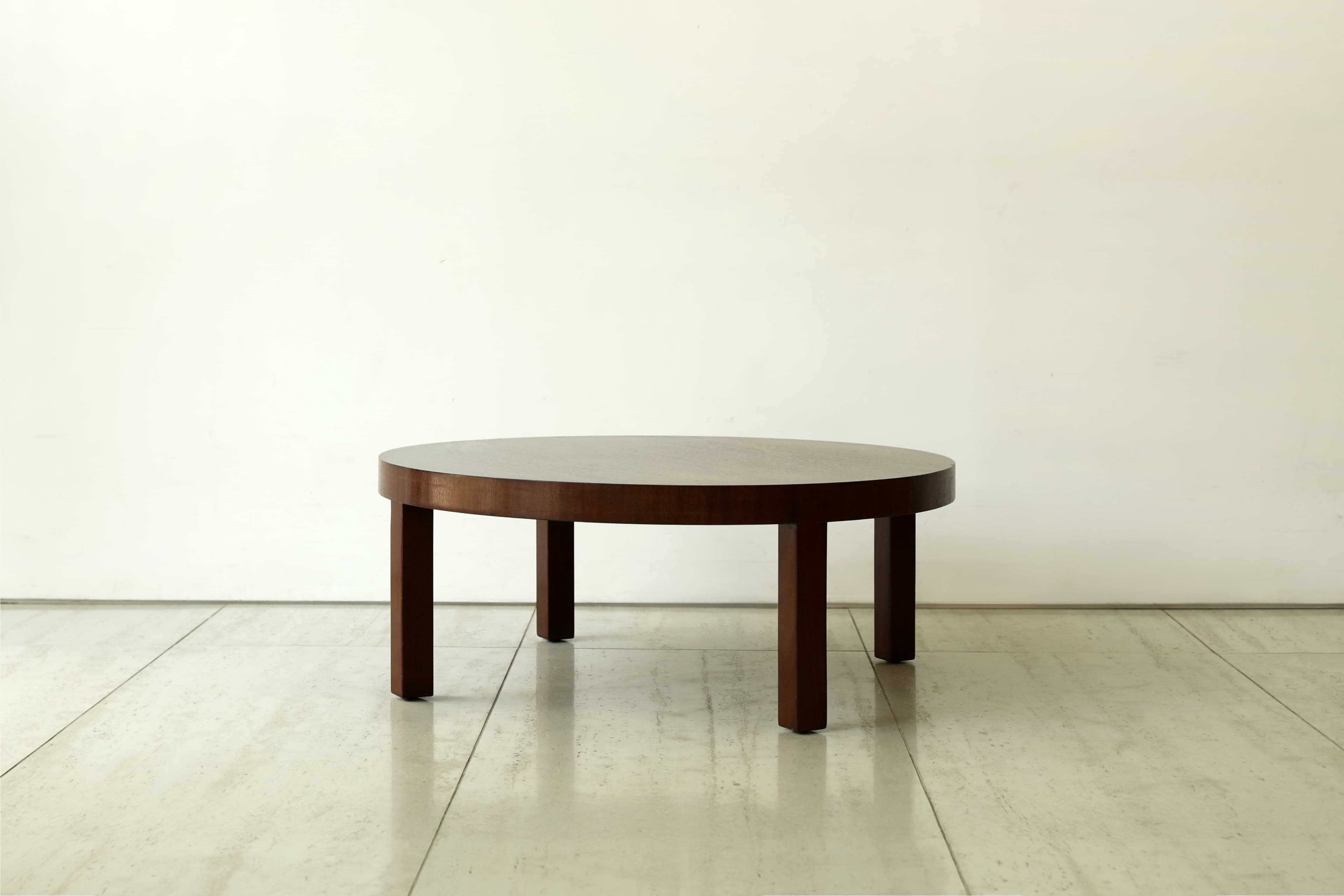 A minimalist round coffee table crafted from dark wood, featuring a thick circular top supported by four sturdy, rectangular legs. The design is simple and functional. — 3D model