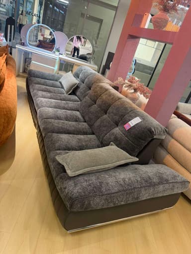 A modern two-tone sofa featuring a dark gray base and lighter gray fabric for the seat and back cushions. The seat and back cushions are distinctively tufted, creating a structured yet plush appearance. Two small, lighter gray rectangular accent pillows are included. The armrests are integrated into the overall low-profile design, blending seamlessly with the seat structure. The sofa rests on a subtle, possibly chrome-finished, minimalist base. — 3D model