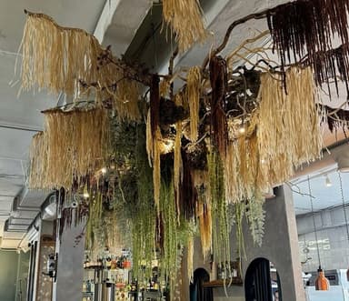 A large, multi-layered ceiling light fixture composed of intertwined natural branches and various cascading botanical elements. It features long, fibrous materials in beige, brown, and green, resembling dried grasses and foliage, with integrated light sources providing ambient illumination from within the dense structure. — 3D model