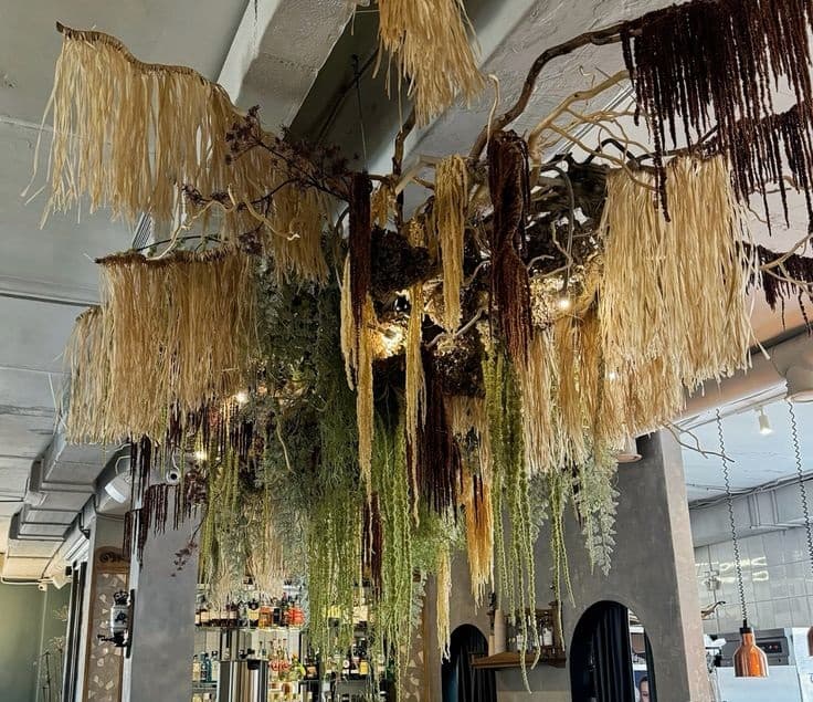A large, multi-layered ceiling light fixture composed of intertwined natural branches and various cascading botanical elements. It features long, fibrous materials in beige, brown, and green, resembling dried grasses and foliage, with integrated light sources providing ambient illumination from within the dense structure. — 3D model