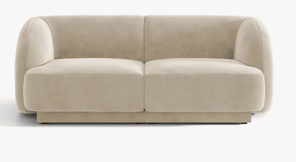 A contemporary two-seater sofa featuring soft, rounded arms and backrest that curve continuously from the base. The sofa is upholstered in a light beige or cream-colored plush fabric, likely velvet or chenille. It has two distinct seat cushions and two back cushions, presenting a clean, minimalist aesthetic with a low-profile plinth base. — 3D model