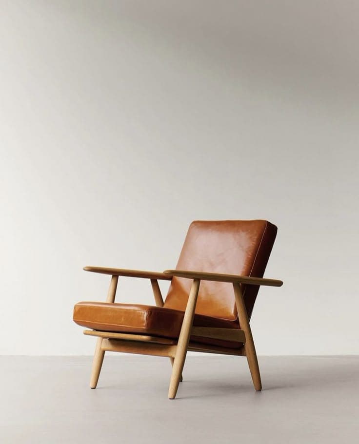 A modern lounge chair featuring a sturdy light-toned wooden frame with visible joinery and comfortable, plush brown leather seat and back cushions. The armrests are simple, rounded wooden bars. — 3D model