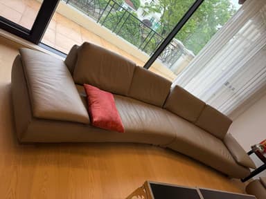 A modern curved sectional sofa upholstered in beige leather, featuring a low profile design and polished metal feet. — 3D model