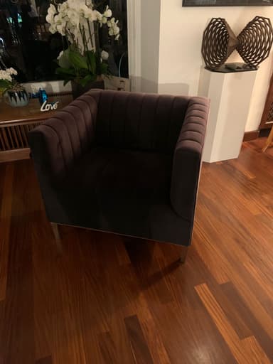 A contemporary upholstered armchair featuring distinctive vertical channel tufting on the interior backrest and inner arms. The chair is clad in a rich, dark plum-colored velvet fabric, presenting a luxurious and soft texture. It has a boxy silhouette with integrated, slightly flared arms, supported by four short, tapered wooden legs in a light finish. The design combines modern aesthetics with a touch of classic elegance. — 3D model