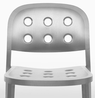 A modern chair with a brushed aluminum finish. It features a curved backrest and seat, both perforated with a pattern of six circular holes each. The chair has four slender, straight legs that taper slightly towards the bottom. — 3D model