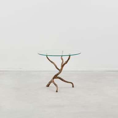 A round glass-topped table with a sculptural base resembling intertwined branches or roots, finished in a textured, aged bronze or brass tone. — 3D model