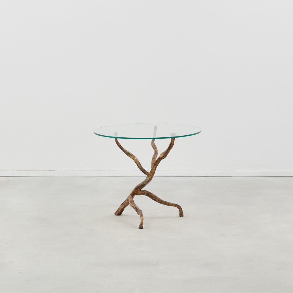 A round glass-topped table with a sculptural base resembling intertwined branches or roots, finished in a textured, aged bronze or brass tone. — 3D model