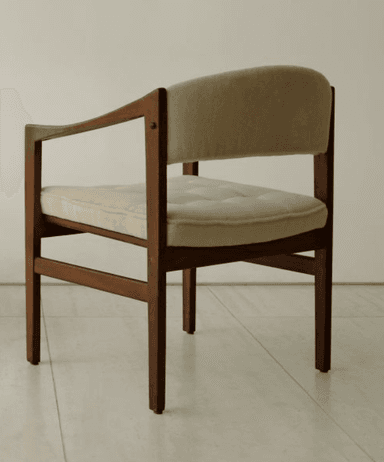 A mid-century modern armchair featuring a dark wood frame and light beige fabric upholstery. The chair has a clean, rectilinear wooden frame with subtly curved armrests. Both the seat and back are padded, with the seat cushion exhibiting button tufting, suggesting a comfortable yet structured design. The wooden legs are straight, and the overall aesthetic is minimalist and functional. — 3D model