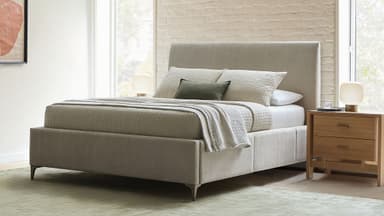 A contemporary upholstered platform bed featuring a soft, neutral-colored fabric. The bed includes a padded, integrated headboard that rises vertically with clean lines. The bed frame is also fully upholstered, creating a seamless and cohesive look. It stands on small, tapered legs, giving it a slightly elevated stance. The design is minimalist and modern, suitable for various bedroom aesthetics. — 3D model