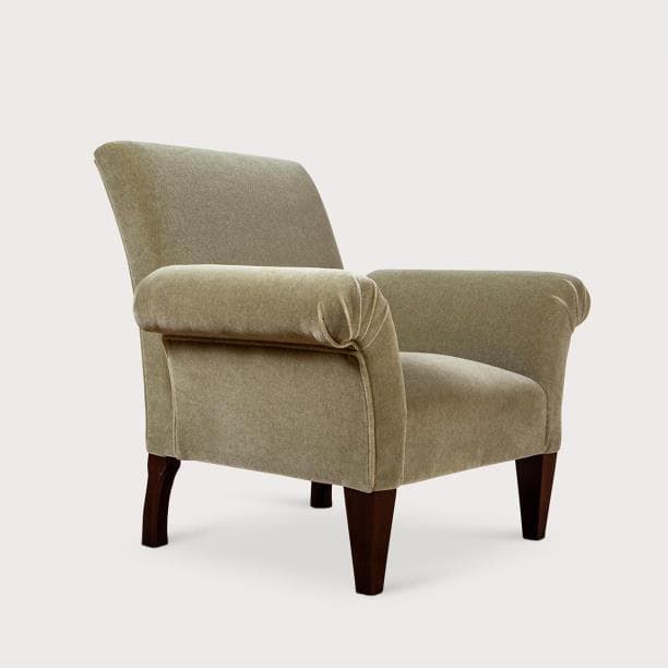 A fully upholstered armchair featuring distinct rolled arms and exposed dark wooden legs. The chair is covered in a soft, plush fabric, likely velvet or velour, in a muted, light greenish-beige color. Its back is gently reclined, and the seat appears well-cushioned, suggesting comfort. The legs are tapered and rectangular. — 3D model