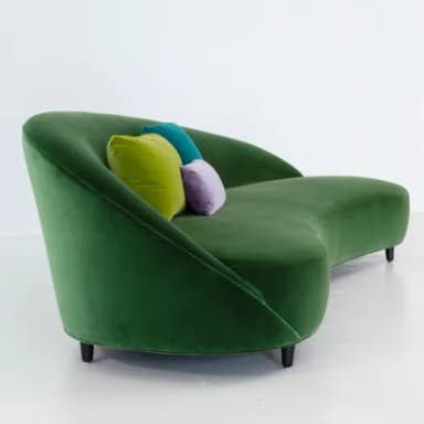 A modern chaise lounge upholstered in rich emerald green velvet, featuring a gracefully curved and ergonomic form. It has a low, integrated backrest that flows seamlessly into the seat and a footrest extension. The piece is supported by discreet, dark cylindrical legs, and three small, round accent pillows in lime green, purple, and teal are placed on the backrest. — 3D model