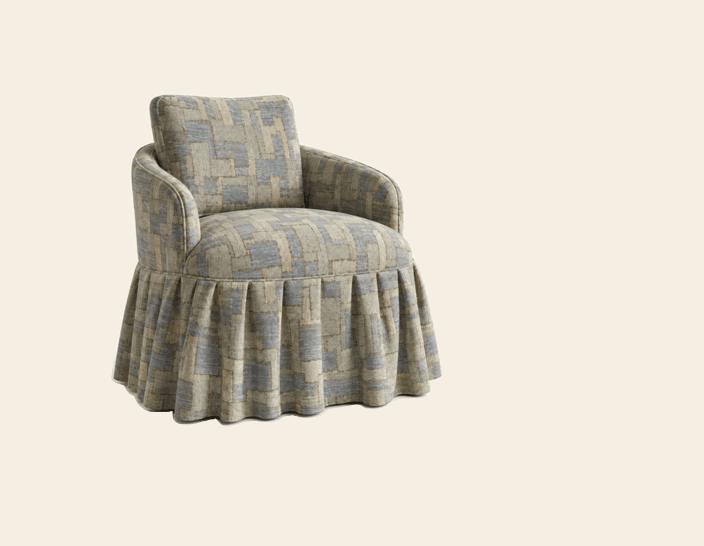 An upholstered tub chair featuring a continuous rounded back and integrated rolled arms, providing a comfortable, enclosed seating experience. The chair is fully covered in a fabric with a distinctive multi-tonal geometric pattern in shades of grey-blue and beige-brown. A full pleated skirt conceals the chair's base, adding a classic and elegant touch to its design. — 3D model