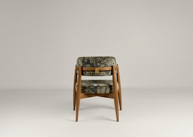 A wooden accent chair with two upholstered seating surfaces. The frame is constructed from light brown wood with tapered legs. The upholstery is a dark fabric with an intricate, possibly embroidered, pattern in a lighter color, featuring scrollwork and geometric motifs. A brass-colored latch or buckle detail is visible on the upper upholstered section. — 3D model