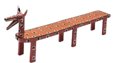 A long, narrow wooden bench featuring a stylized animal head, possibly a fox or dog, at one end. The bench is painted in reddish-orange and off-white colors with black and white spotted patterns across its surface and legs. It is supported by several short, rectangular legs. — 3D model