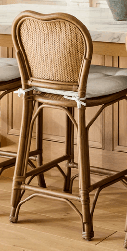 A classic bistro-style bar stool featuring a curved rattan frame and a heart-shaped, tightly woven rattan backrest. The stool includes a light-colored, padded seat cushion secured with white ties. An integrated footrest provides comfort and stability. The natural brown finish of the rattan gives it a warm, inviting aesthetic. — 3D model