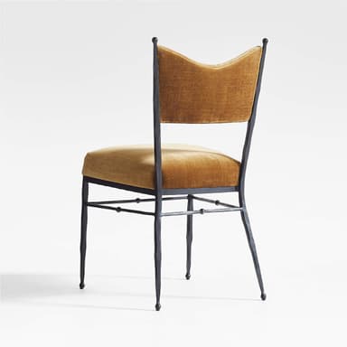 A chair with a dark, metallic frame and a cushioned seat and back. The frame appears to be wrought iron or a similar metal, with four slender legs and a simple stretcher system. The backrest is slightly curved and has a distinctive shape, reminiscent of a butterfly or a stylized 'W'. The upholstery is a rich, golden-brown velvet fabric. — 3D model