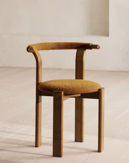 A modern armchair featuring a curved wooden frame with an upholstered backrest and seat. The frame is a medium-toned wood, possibly walnut or oak, with a smooth finish. The backrest is a continuous curved piece that also forms the armrests, capped with small cylindrical wooden details at the ends. Both the backrest and the round seat cushion are upholstered in a textured, mustard yellow boucle fabric. — 3D model