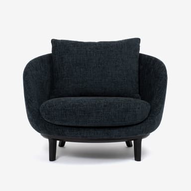 A modern armchair with a rounded, enveloping silhouette. The chair features a deep seat, a low-profile backrest, and integrated armrests that flow seamlessly into the body of the chair. A separate square cushion is placed against the backrest for added comfort. The chair is upholstered in a textured dark blue or charcoal fabric and rests on a dark, possibly wooden or metal, base with four short, tapered legs. — 3D model