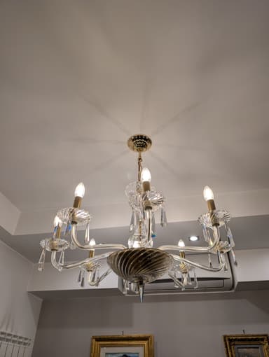 A multi-tiered chandelier with eight arms, featuring clear glass elements and crystal pendants. The central body has a twisted glass design, and the arms are curved, supporting candle-style light bulbs. The hardware appears to be gold-toned. — 3D model