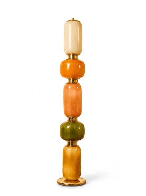 A tall, slender floor lamp featuring a stack of five distinct, translucent art glass segments connected by brass fittings. The segments alternate between elongated cylindrical and more bulbous spherical forms. The color palette includes cream, vibrant orange, peach, olive green, and a warm amber, creating a gradient effect. It stands on a circular brass base. — 3D model