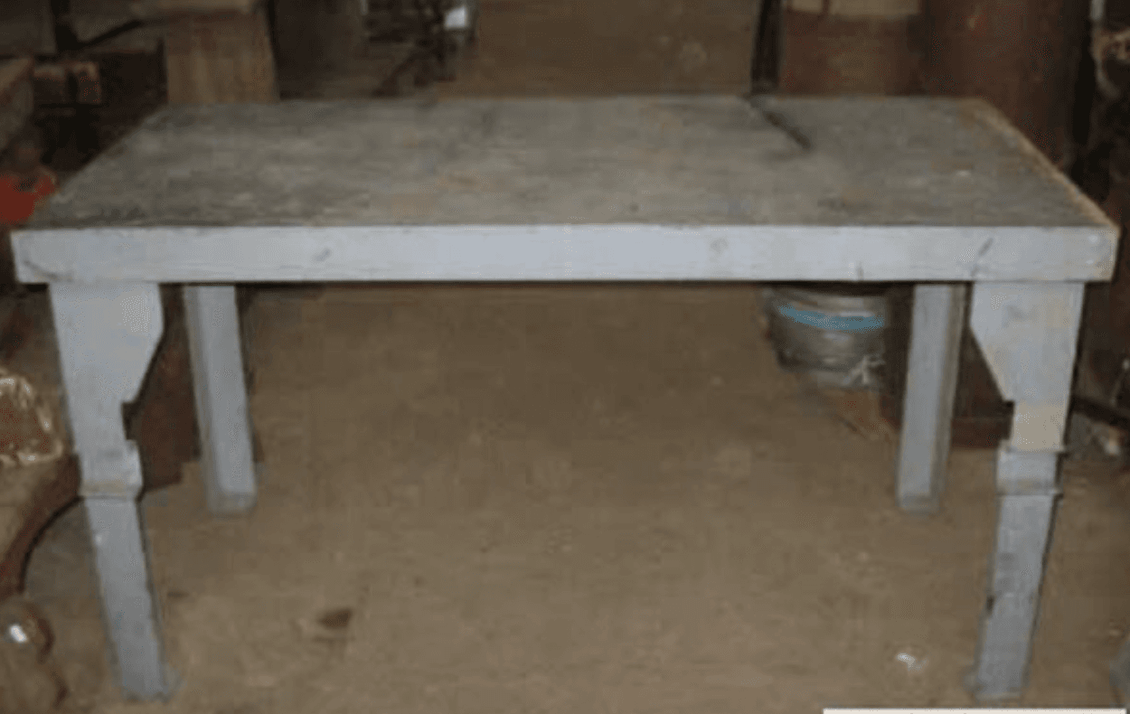 A rectangular dining table constructed from a solid, grey, textured material resembling concrete or stone. The table features a thick rectangular tabletop supported by four substantial, column-style legs that include subtle decorative square blocks near their tops and bases, giving a robust yet refined appearance. — 3D model