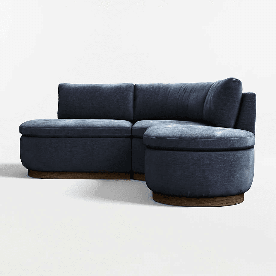 A modular sectional sofa upholstered in a dark blue textured fabric. The configuration includes at least two seat modules and a corner unit with a rounded chaise extension. The base of the sofa features a dark wood trim, likely veneer, with a slight curve that complements the overall design. The cushions are plush, and the backrests are integrated into the seat modules, with one angled backrest on the corner unit. — 3D model