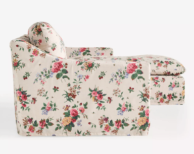 A cream-colored sofa upholstered in a floral fabric with a pattern of roses, peonies, and other flowers in shades of pink, yellow, green, and red. The sofa features a low profile with a slightly sloped armrest. The upholstery covers the entire structure, including the base, cushions, and back. — 3D model