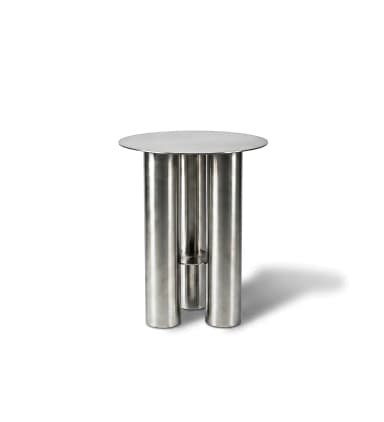 A small, round accent table constructed entirely from brushed stainless steel. It features a circular top supported by three large, cylindrical legs. One of the legs appears to be composed of two half-cylinders or has a vertical cutout, revealing a smaller internal cylindrical element or a void, adding a distinctive design element. The overall aesthetic is minimalist, modern, and industrial. — 3D model