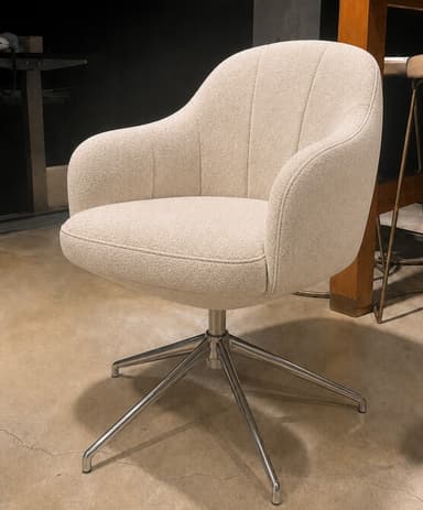 An upholstered armchair with a rounded, shell-like form, integrated armrests, and a fluted back. It features a swivel mechanism and a polished metal four-star base with splayed legs. The upholstery is a light beige, subtly patterned fabric. — 3D model