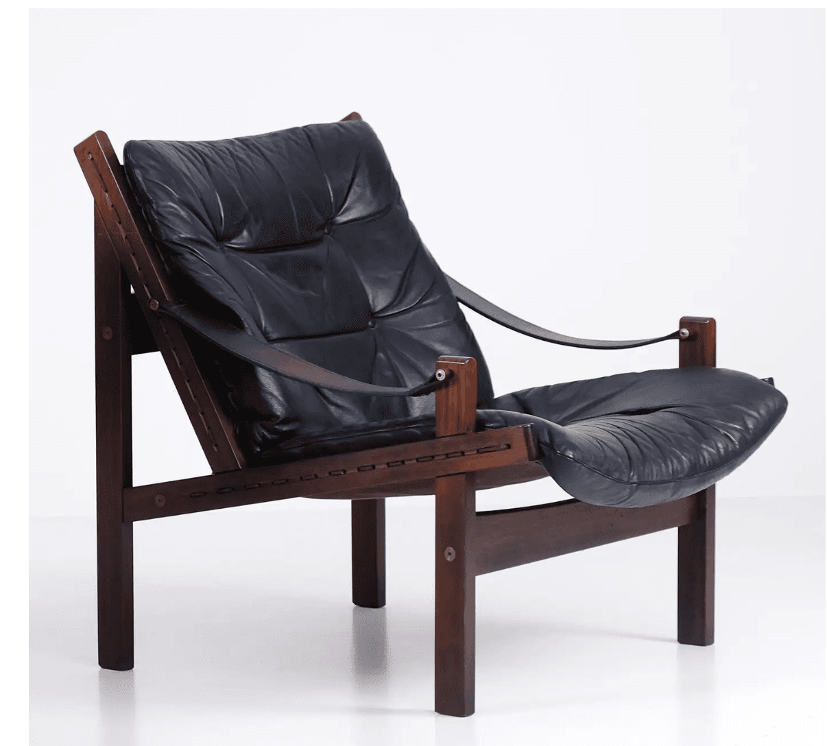 A low-slung lounge chair featuring a dark-stained solid wood frame, likely rosewood, with exposed joinery. It is fitted with thick, tufted black leather cushions for both the seat and back, suspended within the frame. Leather straps form the armrests, secured by brass hardware. — 3D model