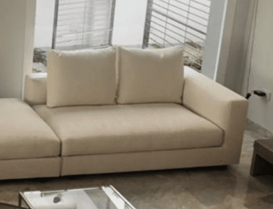 A contemporary modular sectional sofa featuring light-colored fabric upholstery, comprising a main seating unit with a broad armrest and back cushions, and an integrated chaise lounge extension. The design emphasizes clean lines and a minimalist aesthetic. — 3D model