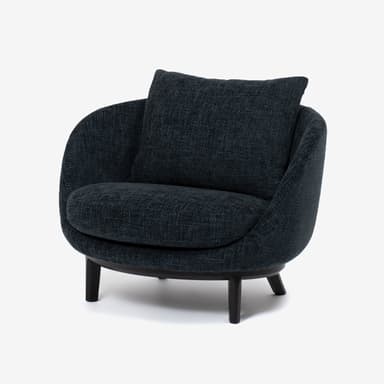 A modern armchair with a rounded, enveloping silhouette. The chair features a deep seat, a low-profile backrest, and integrated armrests that flow seamlessly into the body of the chair. A separate square cushion is placed against the backrest for added comfort. The chair is upholstered in a textured dark blue or charcoal fabric and rests on a dark, possibly wooden or metal, base with four short, tapered legs. — 3D model