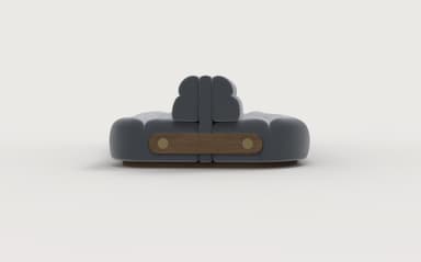 A modern, low-profile sofa with a rounded, modular design. The upholstery appears to be a soft, textured fabric in a muted gray tone. The sofa features deep cushioning with segmented sections on both the seat and the backrest, creating a plush, inviting appearance. The frame is low and appears to be constructed from wood, with a visible wooden accent panel on each end featuring two circular fasteners. The overall aesthetic suggests contemporary design. — 3D model
